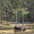 Trampoline with safety enclosure in a wooded backyard surrounded by tall trees and grass