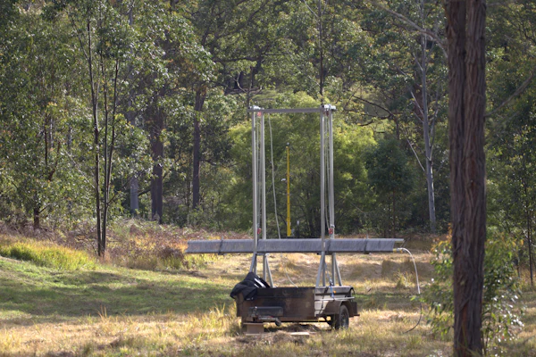Trampoline with safety enclosure in a wooded backyard surrounded by tall trees and grass