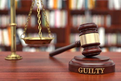 Judge's gavel engraved with 'GUILTY' text on wooden base beside brass scales of justice in courtroom library setting