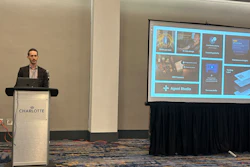 Man speaking at University of Charlotte branded podium during presentation with Agent Studio software interface displayed on screen