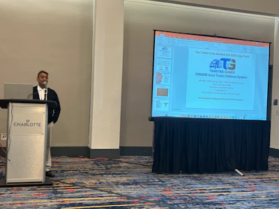 Professional speaker presenting AEG Omni Guard auto trailer defense system at Charlotte conference venue podium.