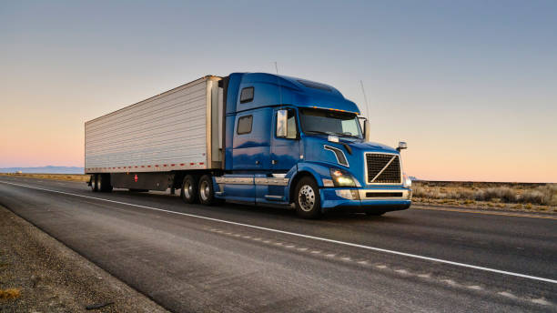 Blue Volvo semi-truck with refrigerated trailer driving on desert highway at sunset