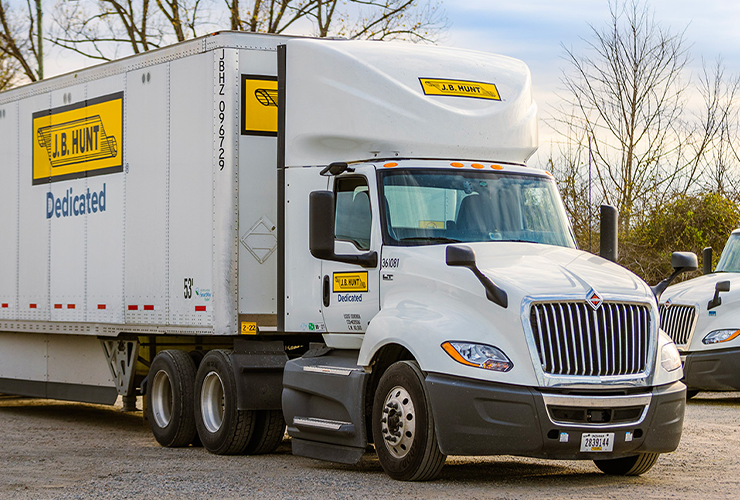 White J.B. Hunt semi-truck with yellow and black branding on the road with bare trees in background
