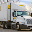 White J.B. Hunt semi-truck with yellow and black branding on the road with bare trees in background