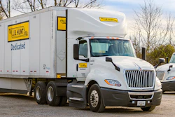 White J.B. Hunt semi-truck with yellow and black branding on the road with bare trees in background