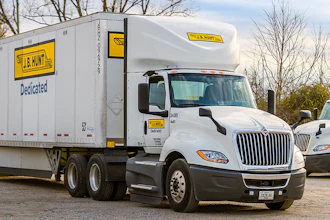 White J.B. Hunt semi-truck with yellow and black branding on the road with bare trees in background