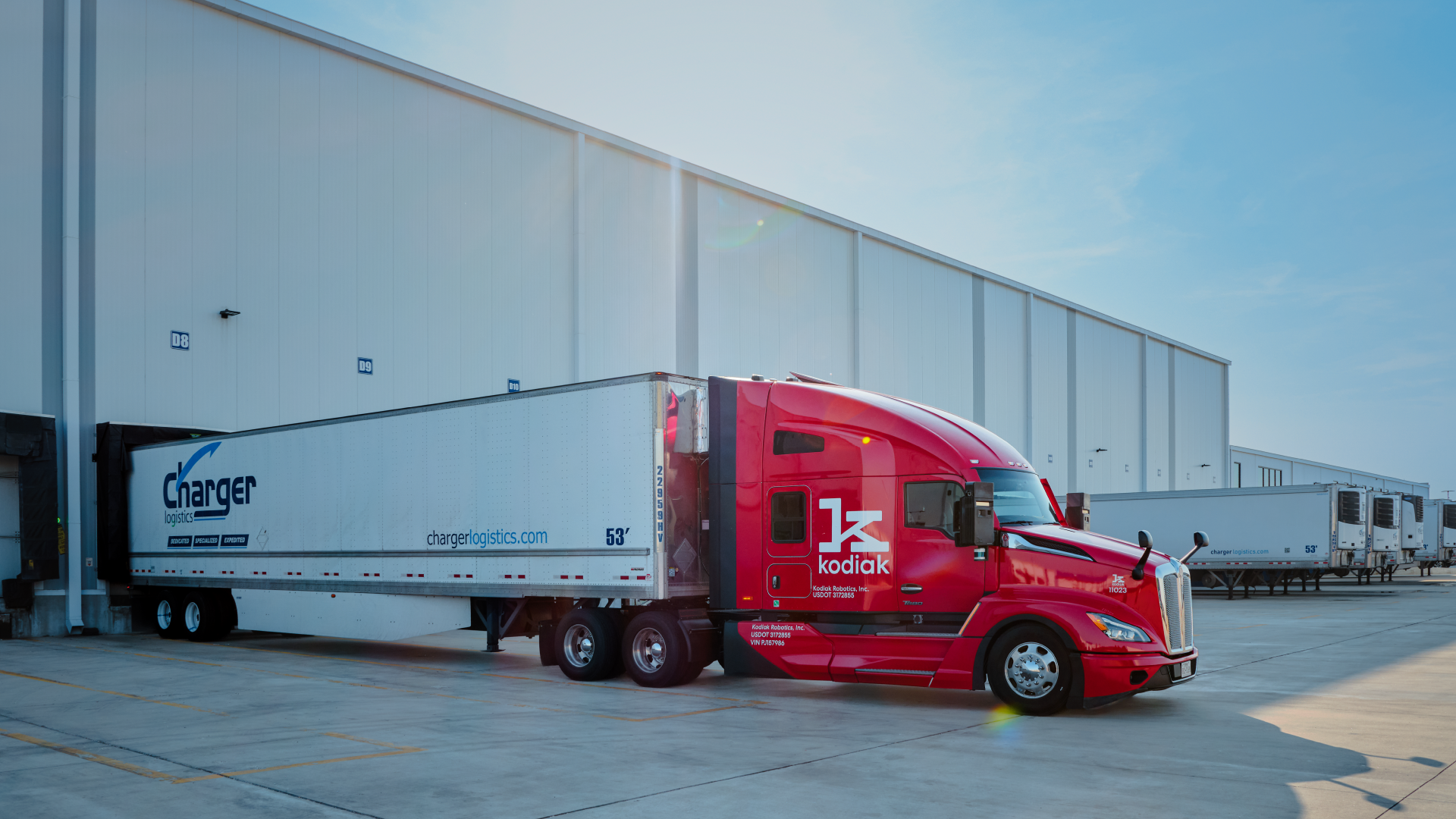 Red Kodiak semi-truck with white Charger Logistics trailer parked at industrial facility