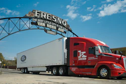 Red semi-truck with white trailer under Fresno's historic welcome sign against blue sky