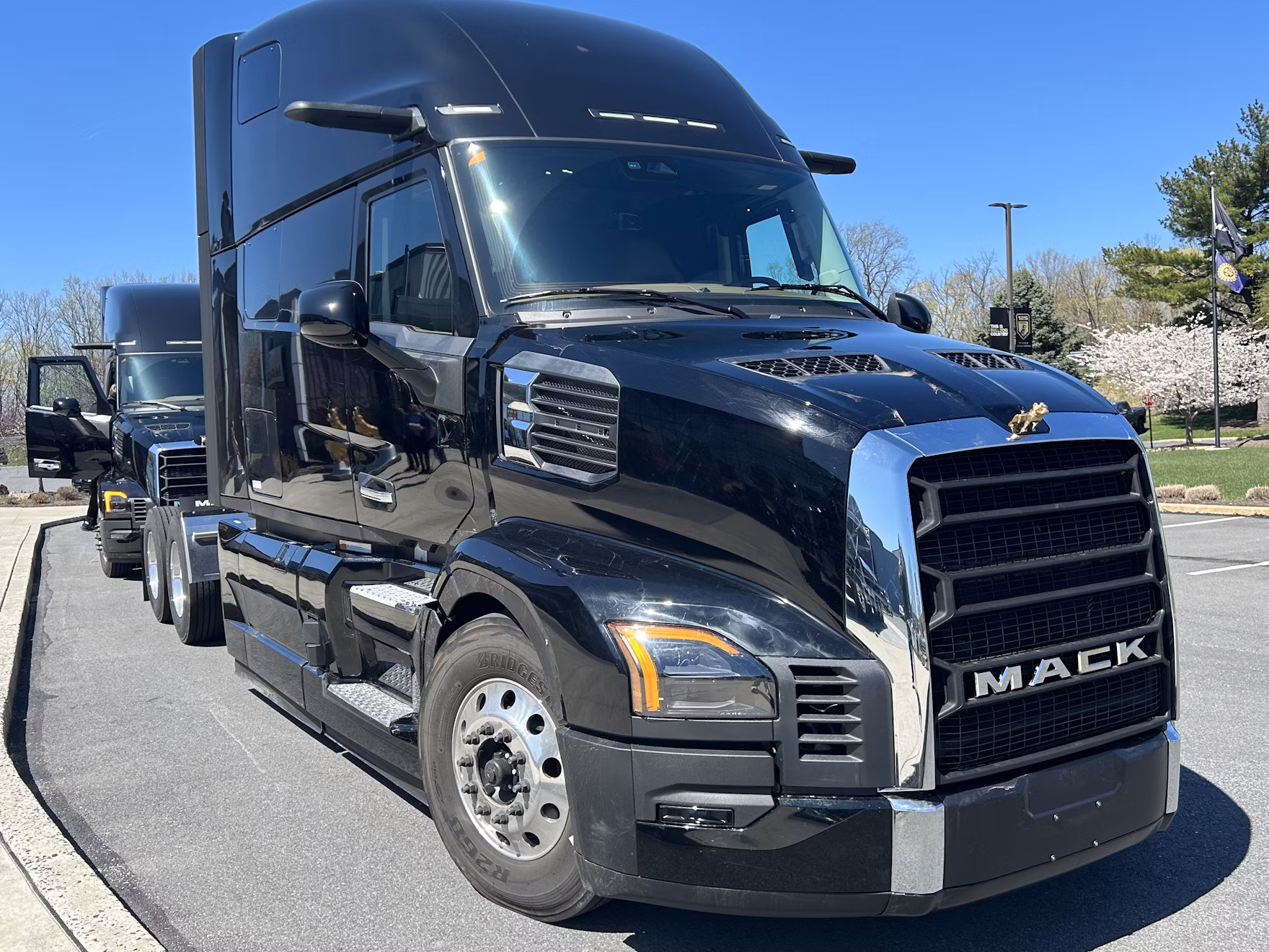 Black Mack semi-truck parked in sunny lot with clear sky and trees in background