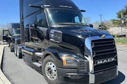 Black Mack semi-truck parked in sunny lot with clear sky and trees in background