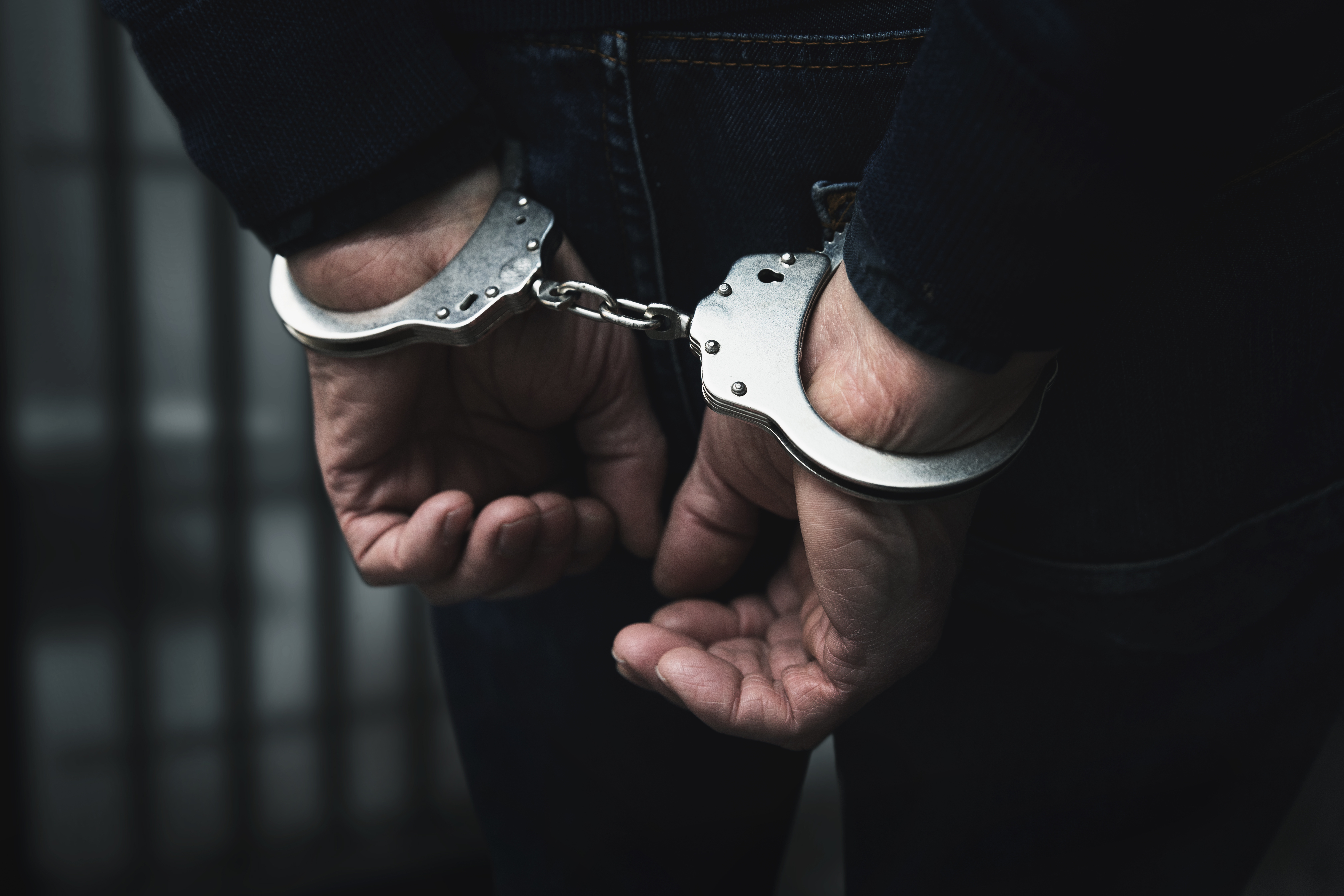 Close-up of hands restrained with metal handcuffs against dark clothing