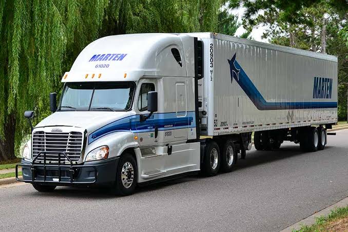White and blue Marten Transport semi-truck with trailer on a tree-lined road