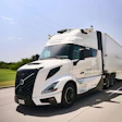 White Volvo semi-truck driving on highway with green landscape and blue sky