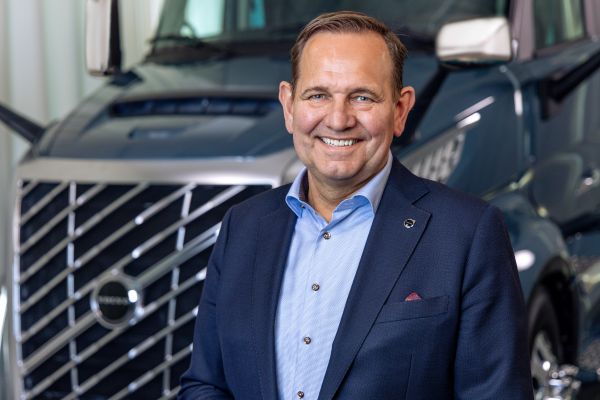 Professional man in navy blazer and light blue shirt smiling in front of commercial vehicles Headshot