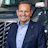 Professional man in navy blazer and light blue shirt smiling in front of commercial vehicles Headshot