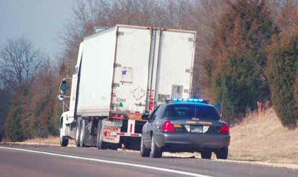 White refrigerated truck and dark sedan driving on highway with bare trees in background