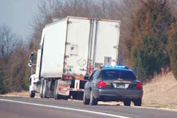 White refrigerated truck and dark sedan driving on highway with bare trees in background
