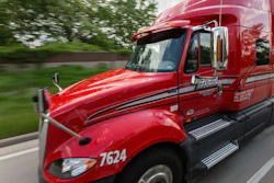 Red Schneider semi-truck with company branding driving on highway with green trees in background