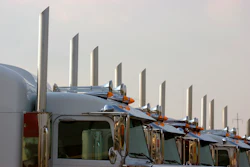 Fleet of semi-trucks lined up showing chrome exhaust stacks and cab designs against overcast sky