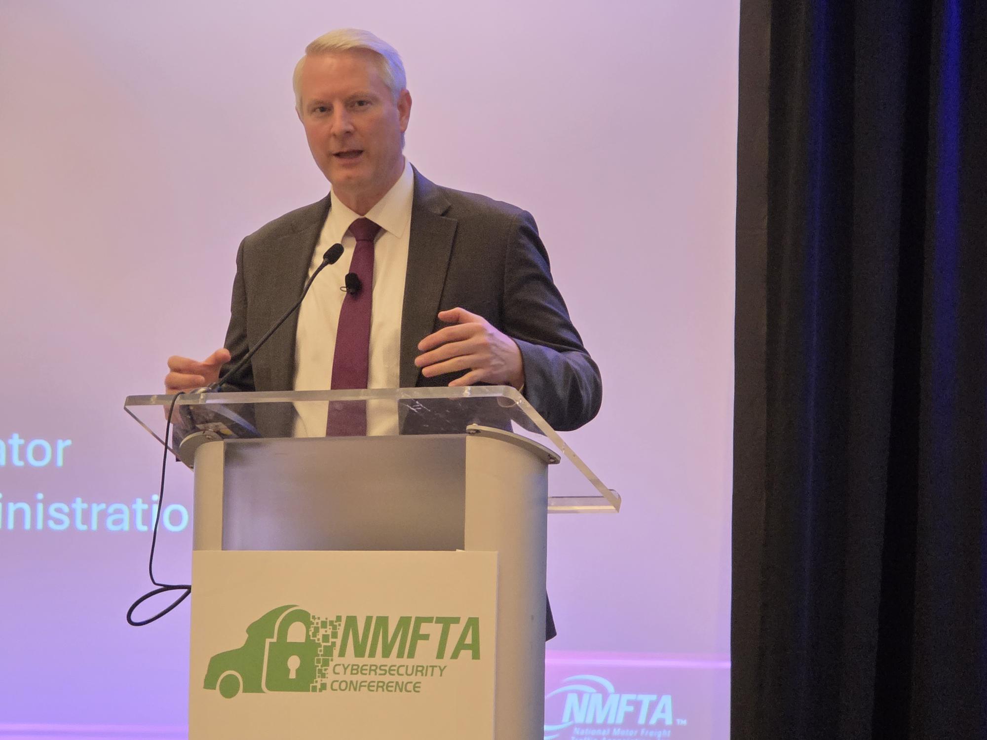 Professional speaker at podium with NMFTA Cybersecurity Conference logo during presentation event