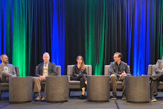 Five professionals seated on stage during a panel discussion with blue and green curtains in background