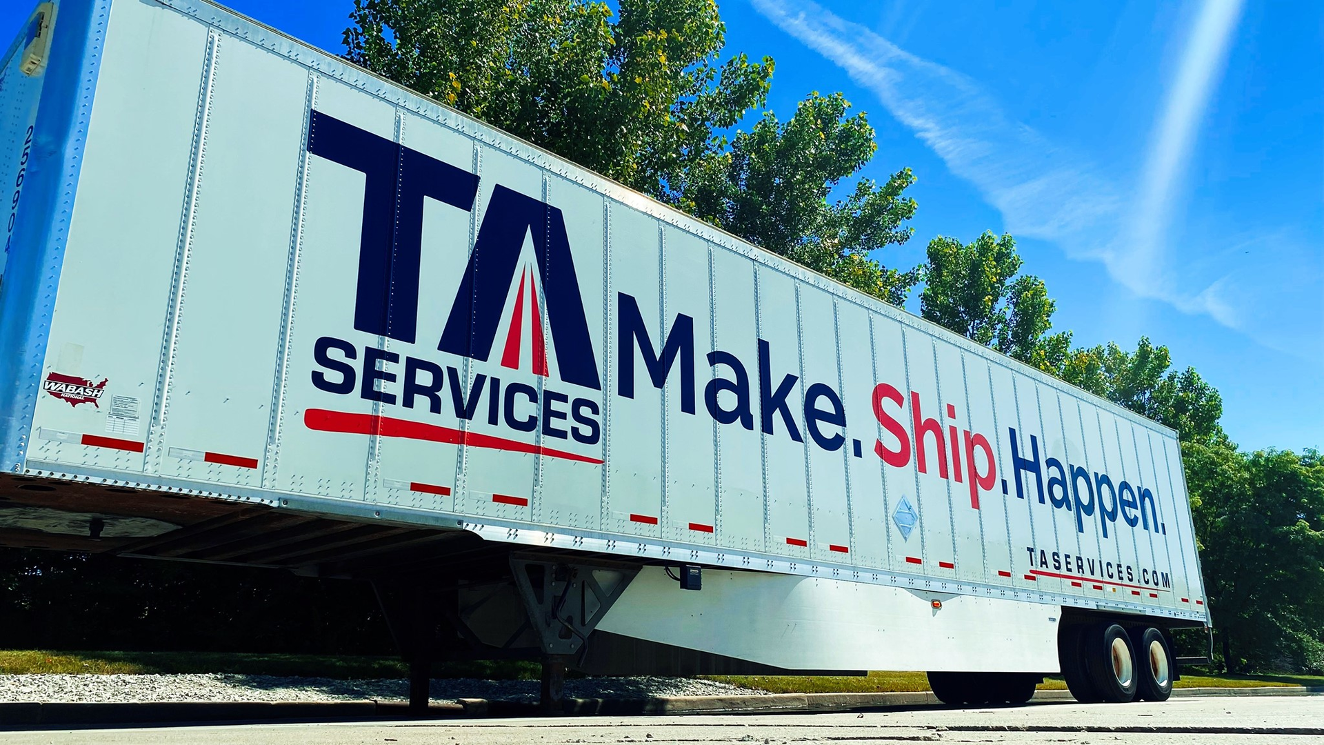 TA Services semi-trailer with 'Make.Ship.Happen' tagline parked against blue sky and trees