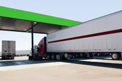 Red semi-truck with white trailer parked under green canopy at industrial loading dock facility