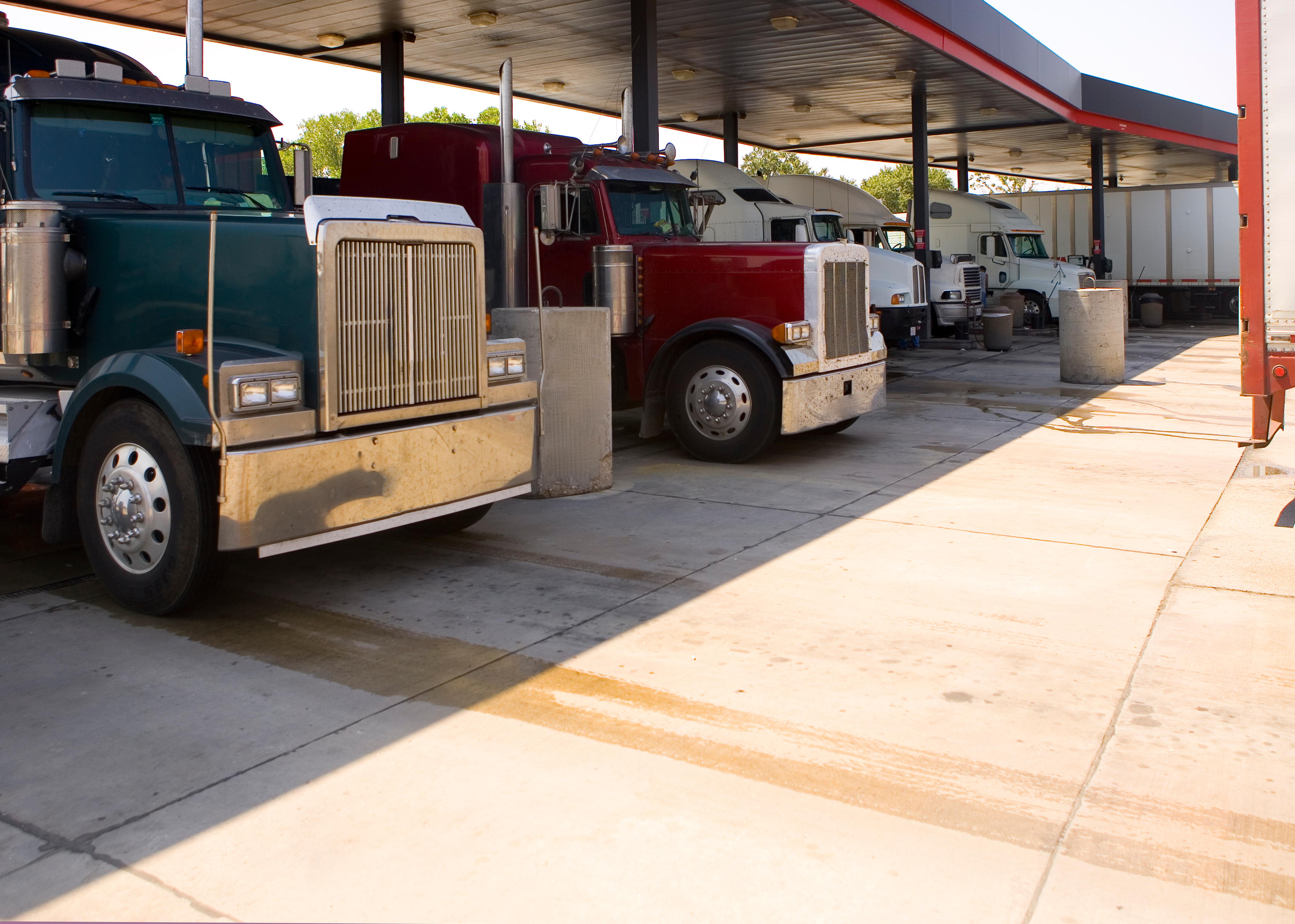 Multiple commercial semi-trucks parked under a covered structure at a truck stop facility