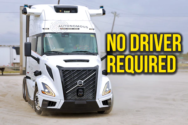 White autonomous semi-truck with 'No Driver Required' text overlay in parking lot