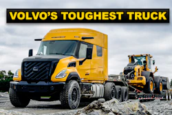 Yellow Volvo semi-truck with construction equipment on gravel site