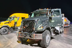Commercial trucks lined up at night, including yellow Volvo and gray Nissan vehicles in fleet formation