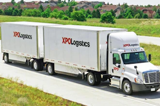 XPO Logistics semi-truck with double trailers driving on highway through suburban landscape