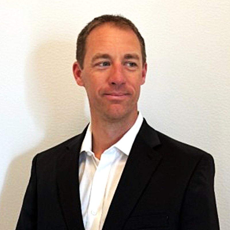 Professional headshot of a man in a black blazer and white shirt against a neutral background Headshot